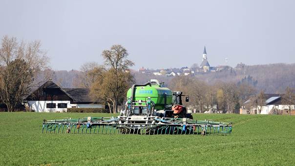 Un tracteur fertilise une parcelle, on voit un village avec une église en arrière-plan